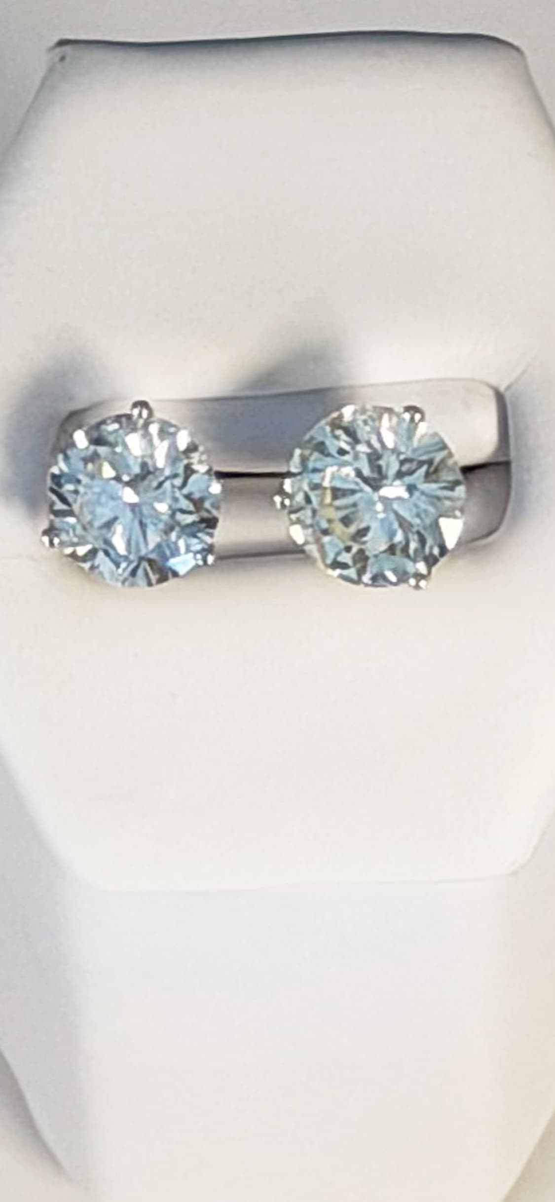 A pair of round brilliant diamond stud earrings on a display stand